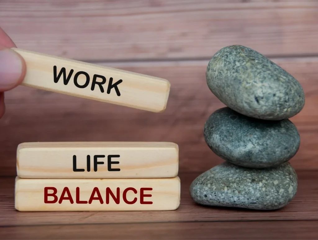 Trækloder stablet med ordene 'work', 'life' og 'balance' ved siden af tre stablede sten.